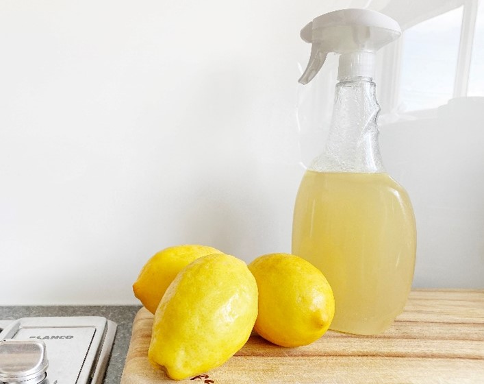 Three Lemons on a cutting board, in front of a lemon filled spray bottle.